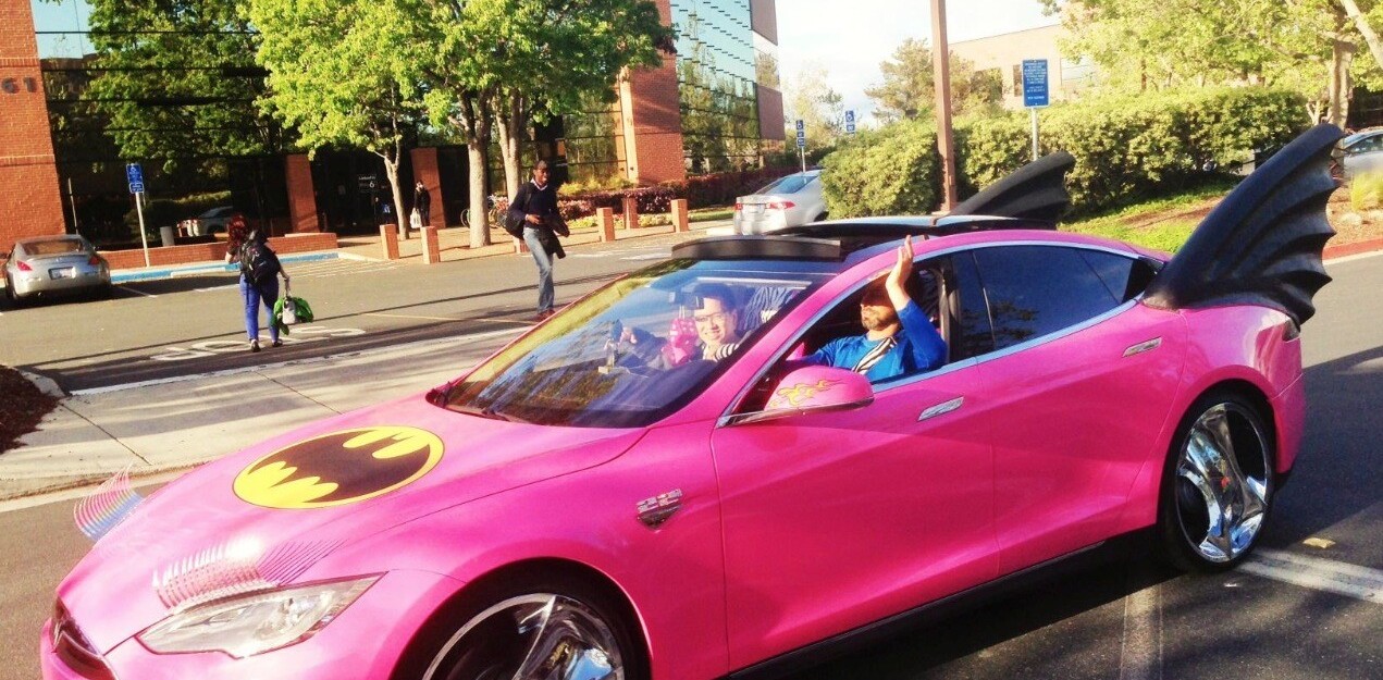 Sergey Brin in Google Glass driving a pink Tesla Batmobile with eyelashes